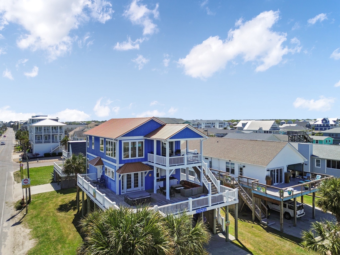 Elevated beachside retreat with vibrant blue siding and multiple decks, perfectly positioned in a charming coastal neighborhood under sunny skies.