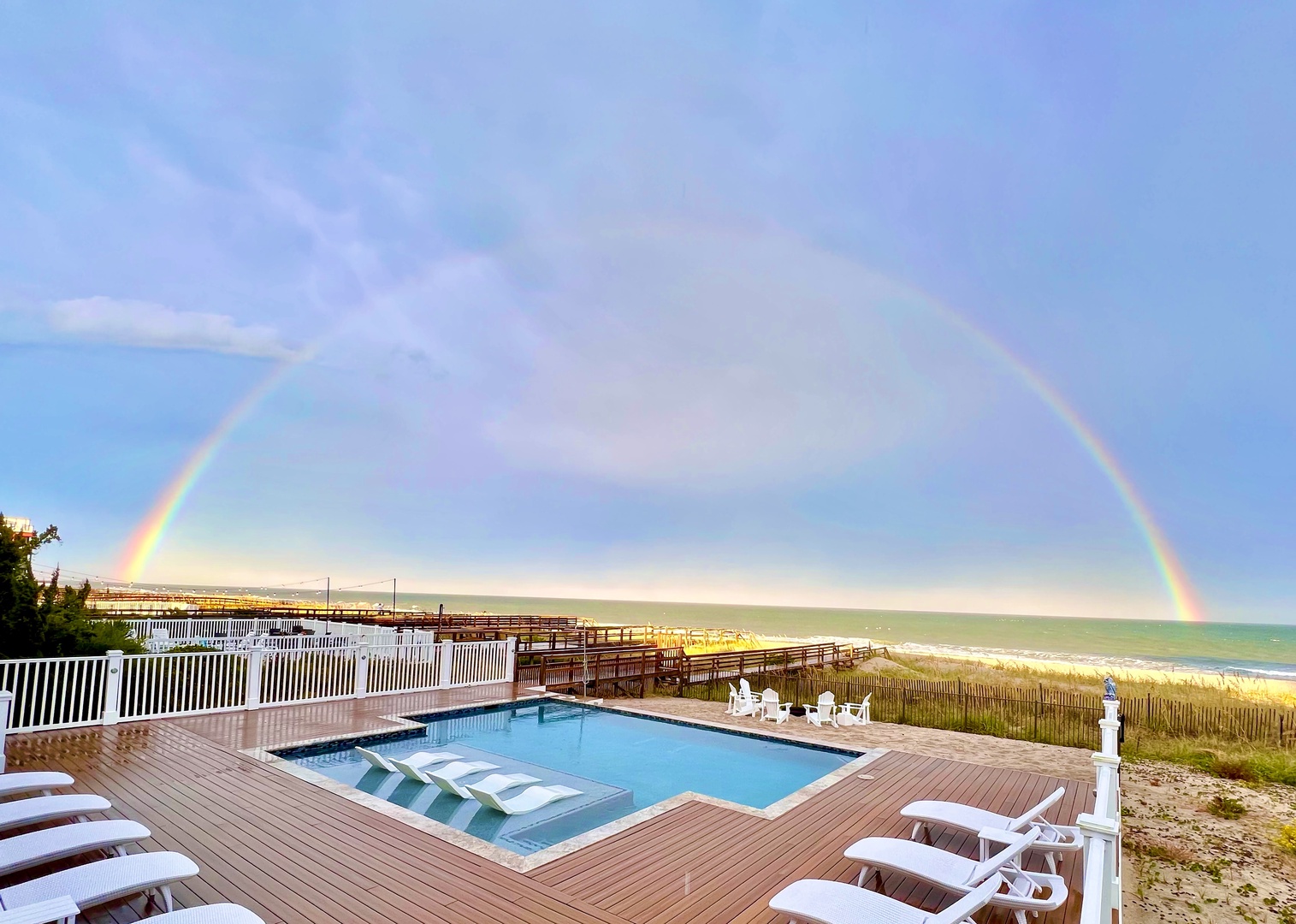 Stunning beachfront property featuring outdoor pool and direct beach access beneath a magnificent rainbow arcing over the coastline.
