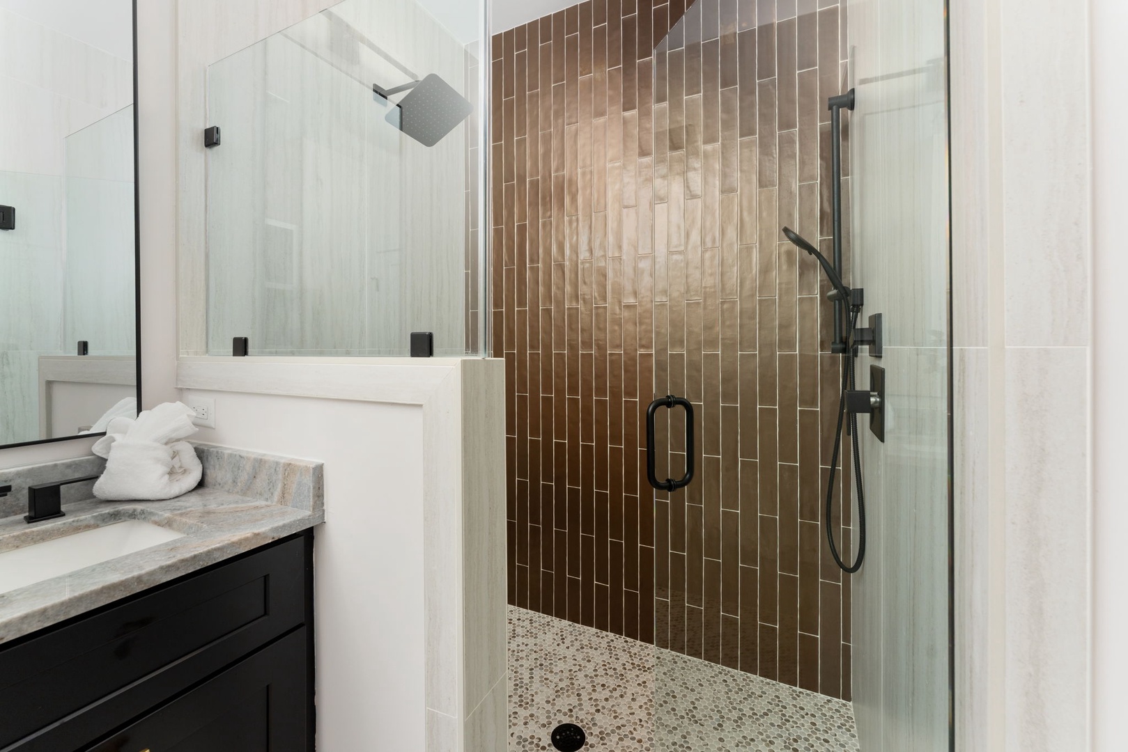 Your spa-like bathroom features a stunning glass-enclosed shower with elegant bronze tiling and rainfall showerhead for ultimate relaxation.