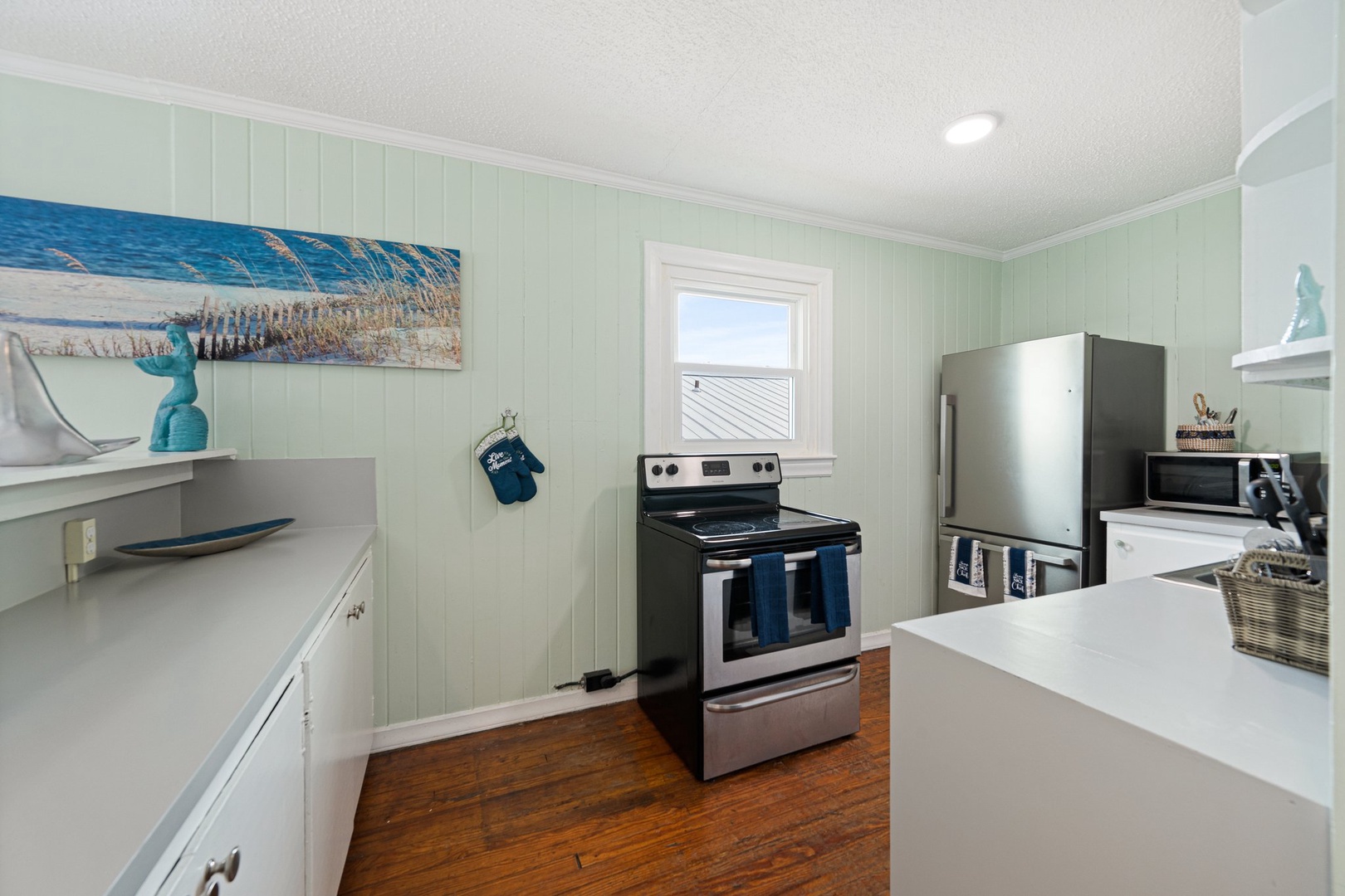 Your fully equipped kitchen features coastal charm with sea-green walls, stainless steel appliances, and beach-themed artwork—perfect for preparing memorable meals.