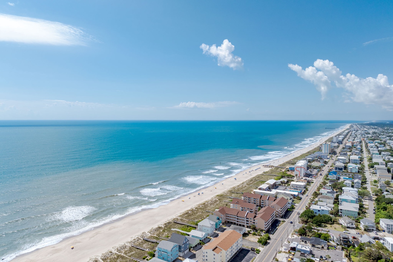 Aerial view showcasing the property's beachfront location along pristine sandy shores and turquoise waters, with the coastal community stretching into the distance under clear blue skies.