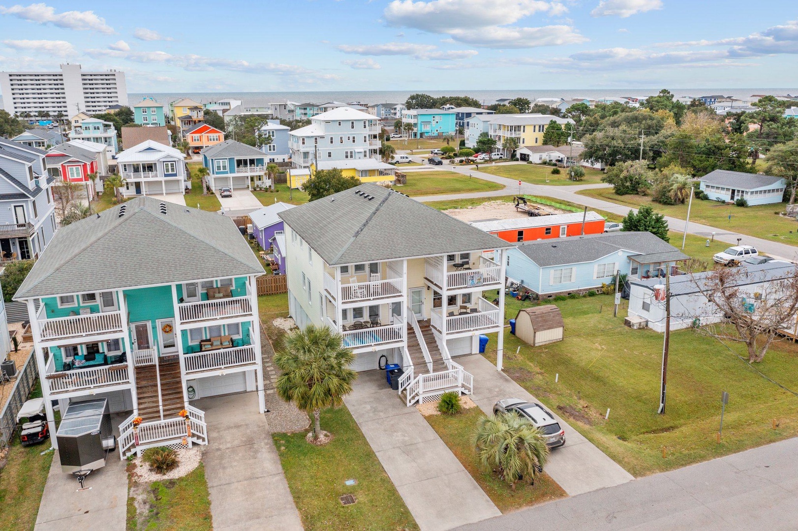 Aerial view of colorful beach houses in a quiet coastal neighborhood, surrounded by green spaces and palm trees.