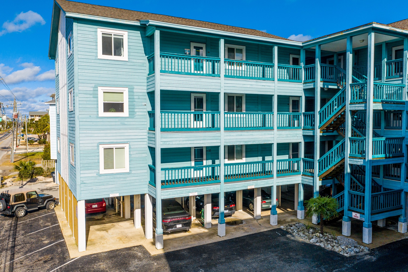 Charming turquoise beach building with multiple balconies and covered parking on the ground level.
