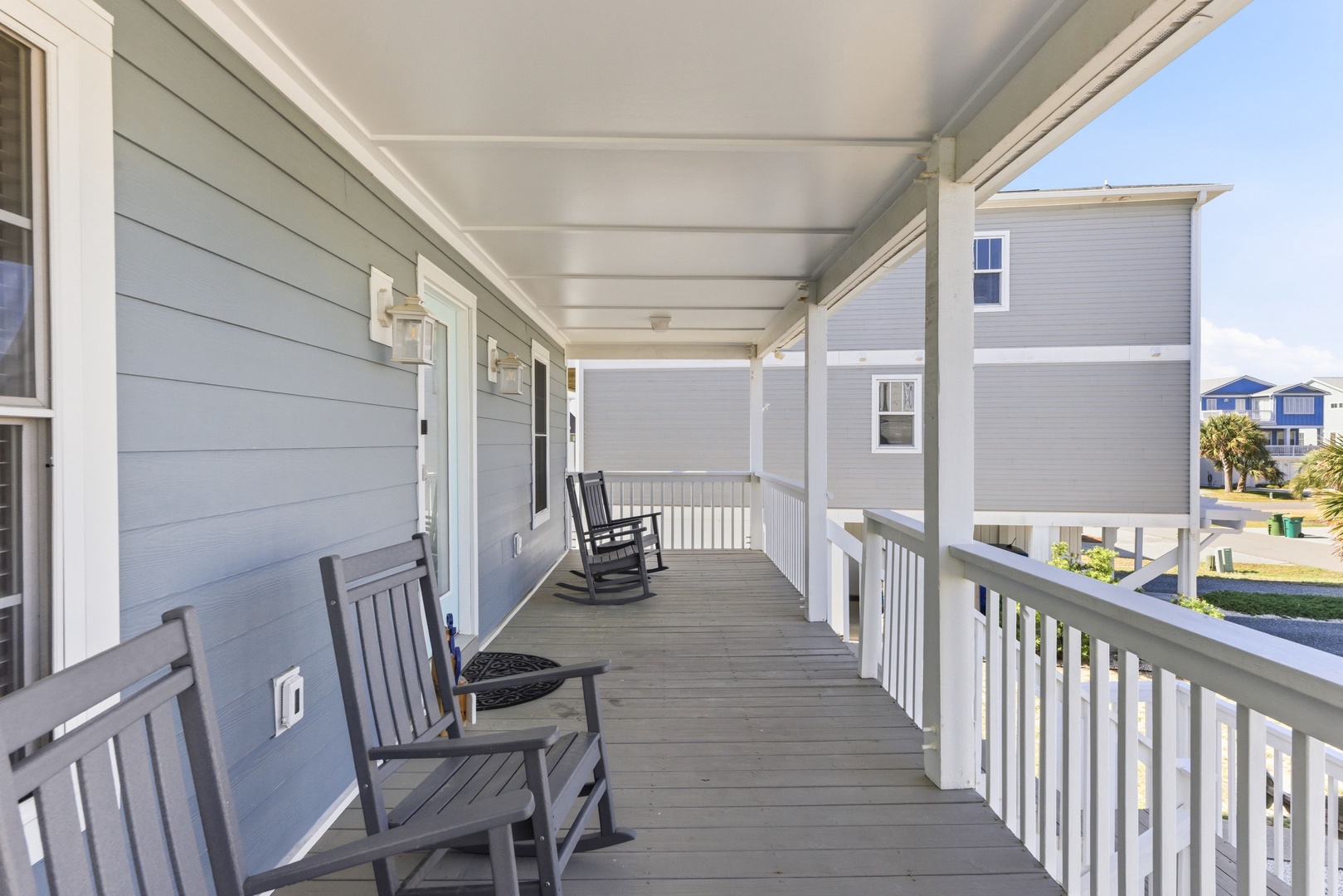A welcoming covered porch with classic rocking chairs offers your quiet spot to unwind, overlooking a peaceful residential neighborhood with coastal charm.
