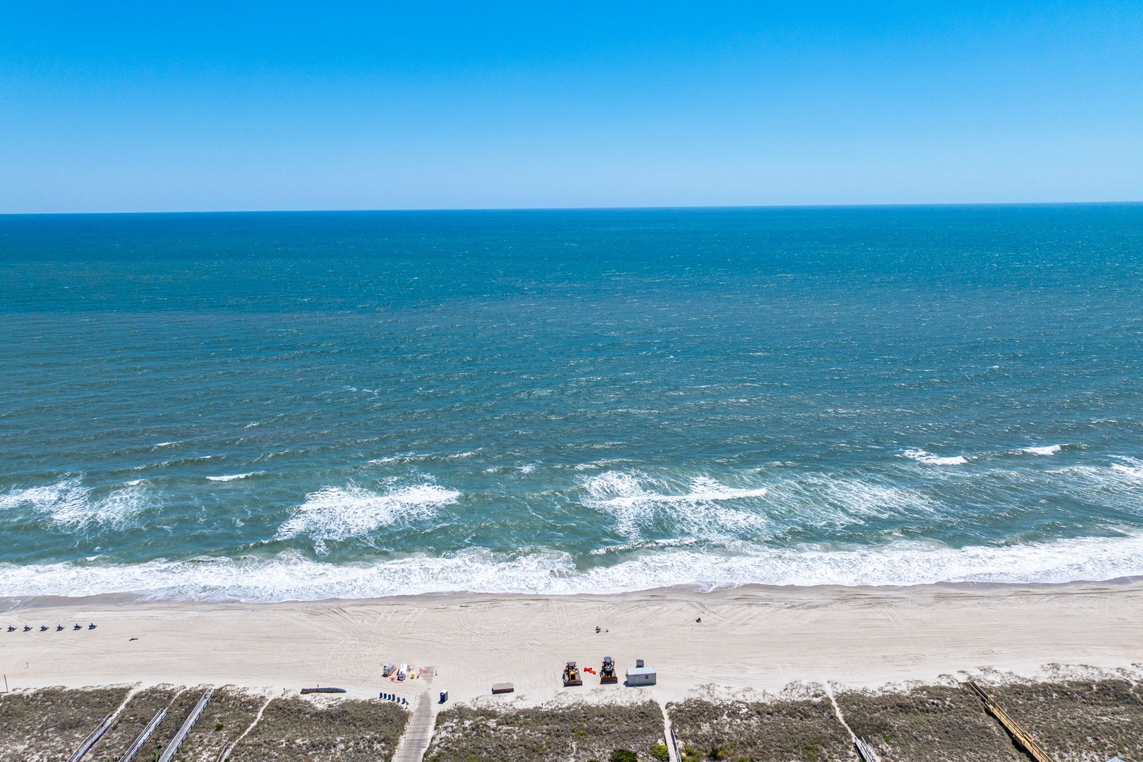 Pristine coastline with rolling waves meeting sandy shores under brilliant blue skies near the property.