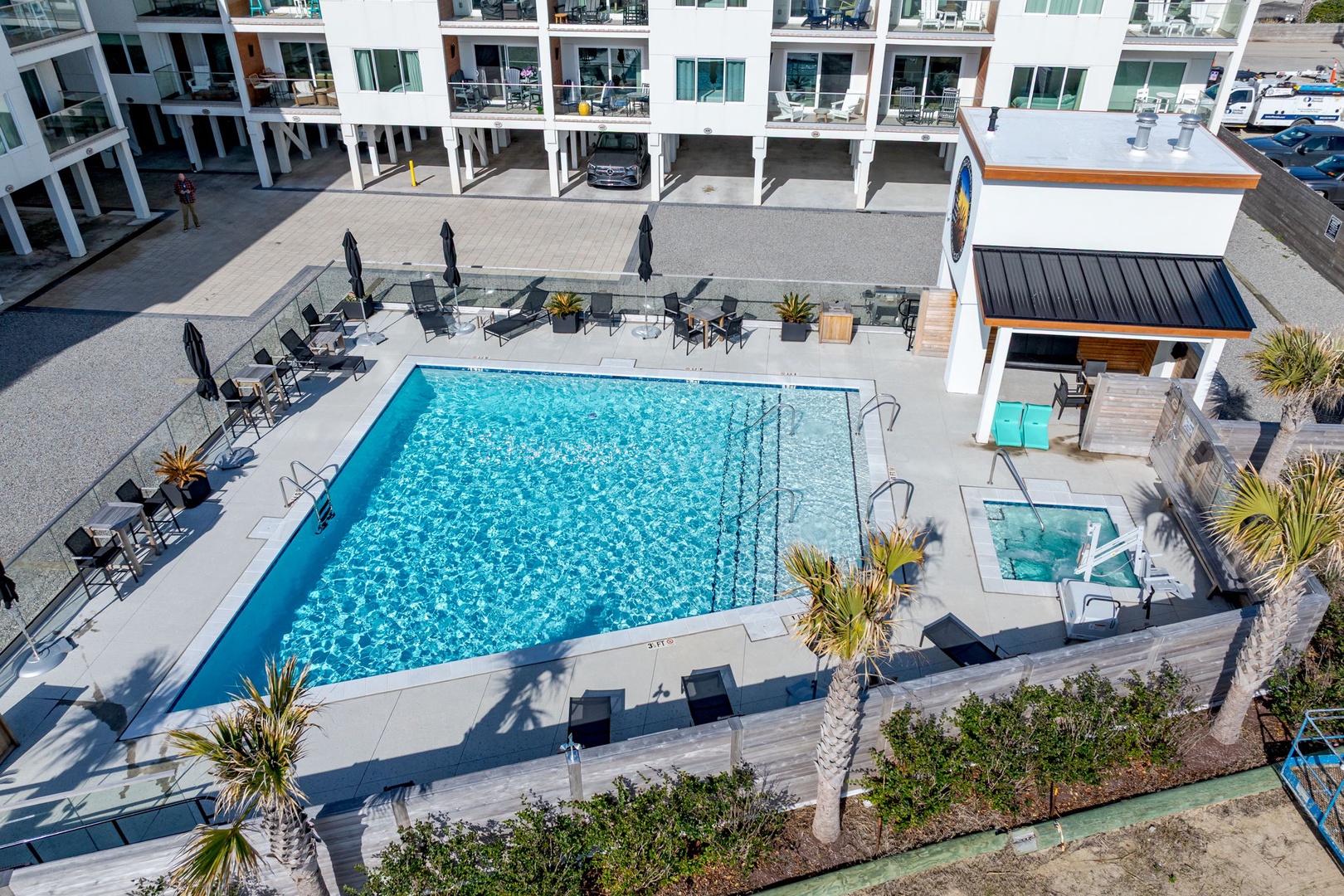 Modern resort pool complex featuring main swimming pool with adjacent hot tub, surrounded by tropical landscaping and contemporary amenities.