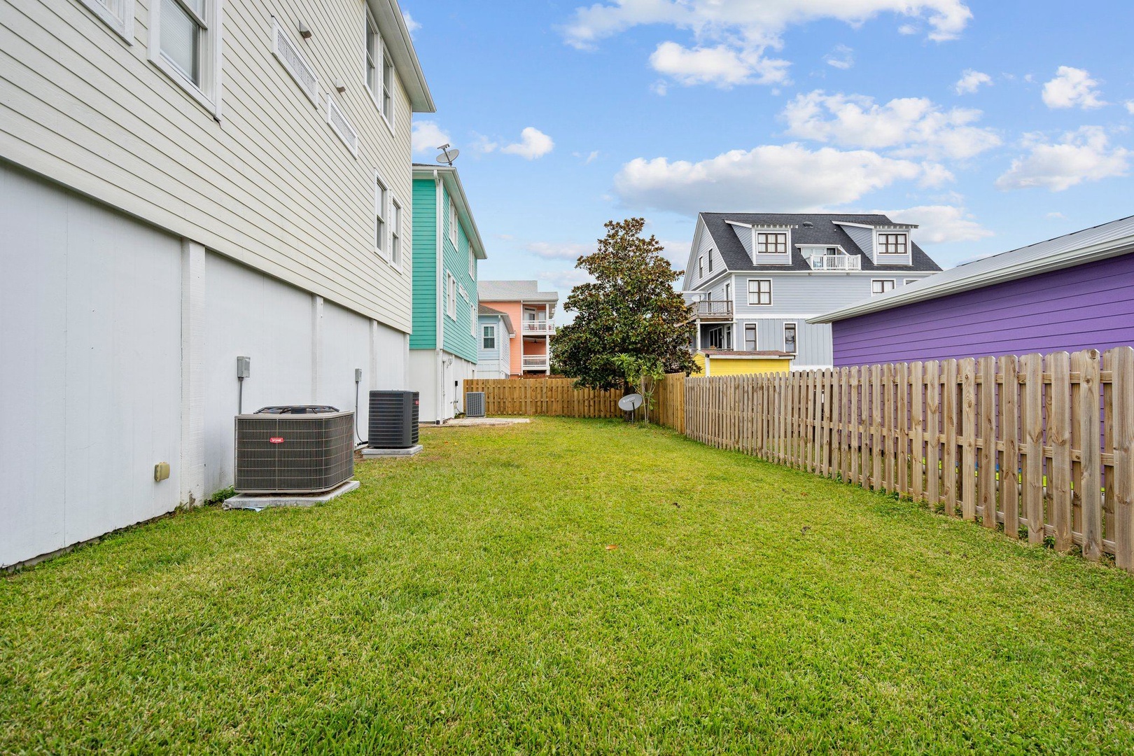Private backyard with fresh green lawn surrounded by colorful neighborhood homes under bright blue skies.