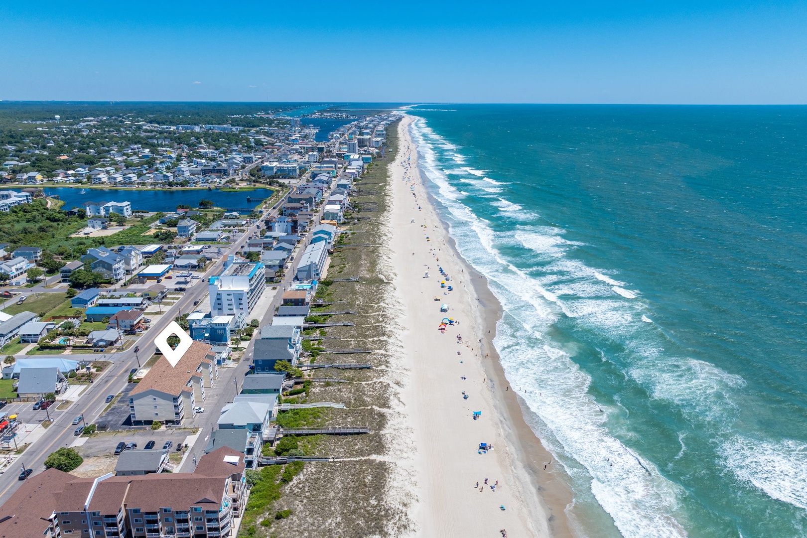 A vibrant coastal community stretches along pristine shores, with turquoise waves rolling onto white sand beaches. The area offers a classic seaside atmosphere with nearby shops and dining.