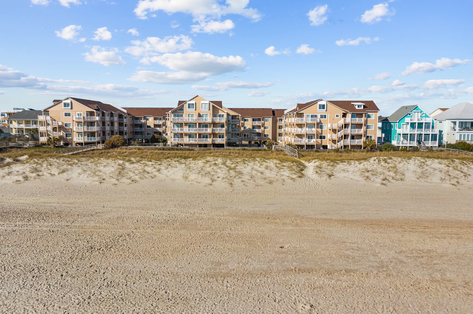 Beachfront property buildings line the sandy shore under a bright blue sky with scattered clouds.