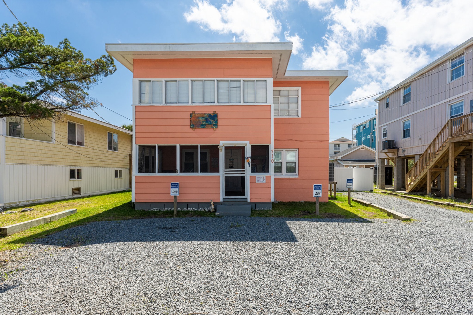 A vibrant coral-colored beach house situated in a quiet coastal neighborhood, featuring modern architecture, ample parking, and nearby beach access.