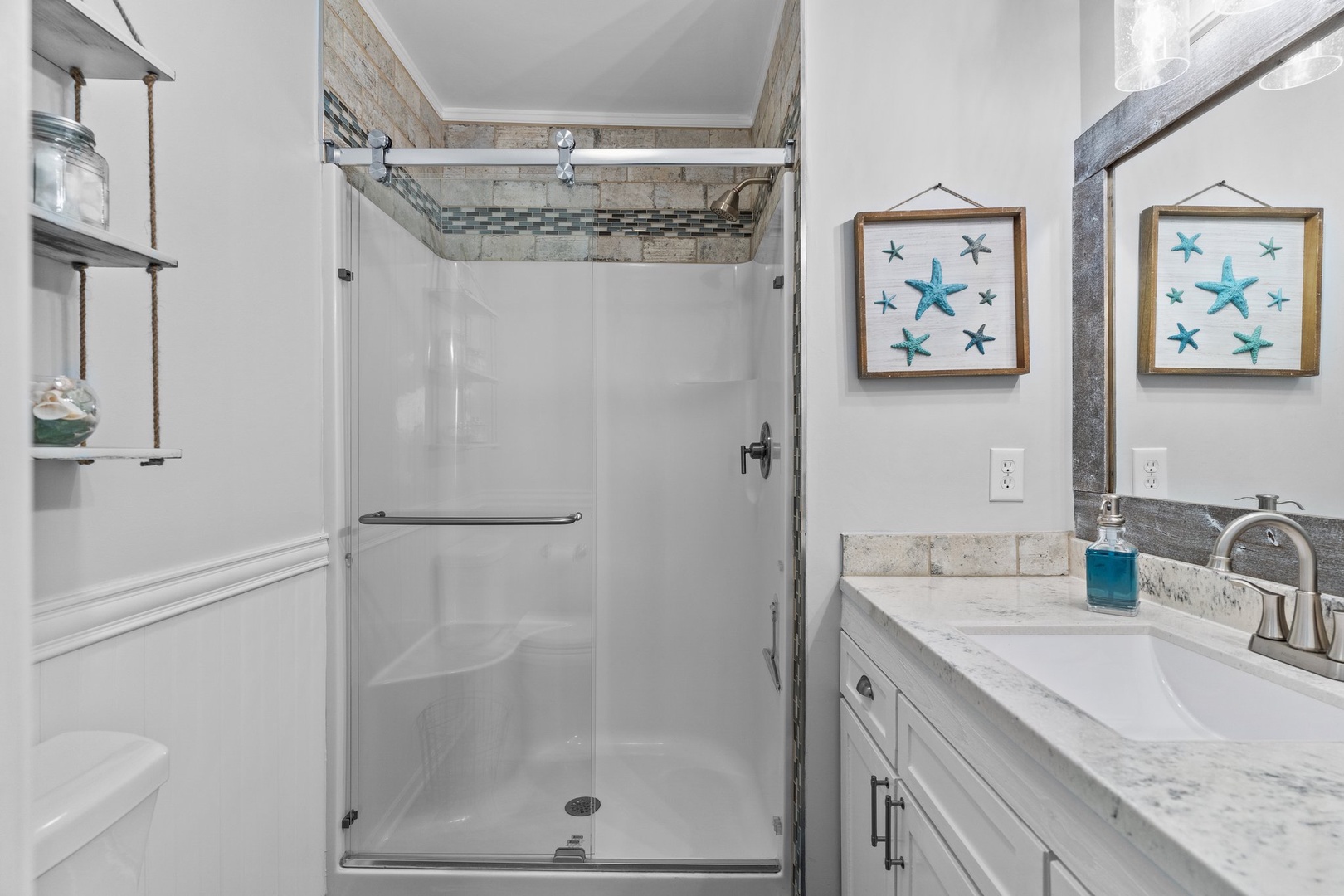 Refresh in your bright bathroom with coastal-themed artwork, spacious shower, and modern vanity.