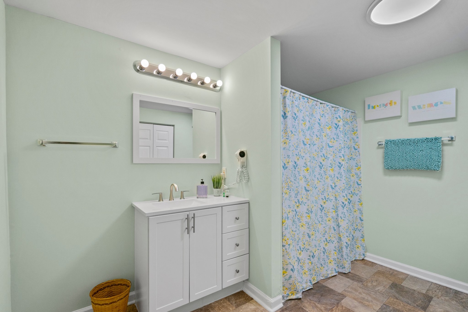 Step into your cheerful bathroom with soft mint walls, bright vanity lighting, and a refreshing floral shower curtain.