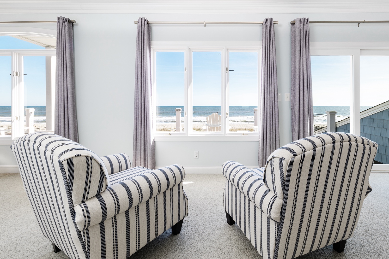Sink into striped chairs and gaze out at endless ocean views through floor-to-ceiling windows in your bright coastal retreat.