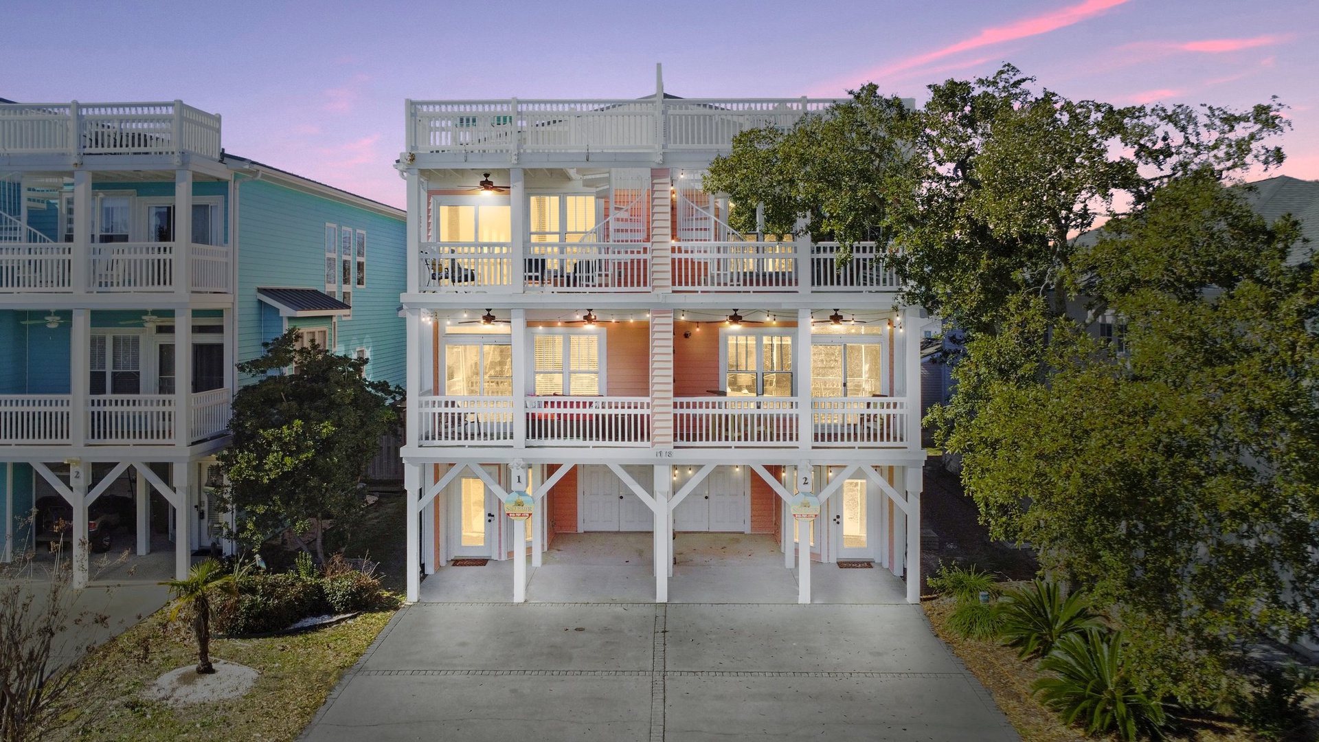 Charming coastal home with warm evening lighting and multiple decks surrounded by mature trees in a peaceful neighborhood.