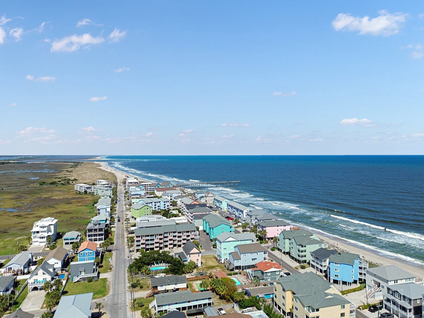 Stunning aerial view of beachfront community with colorful coastal homes stretching along pristine sandy shores and rolling ocean waves.