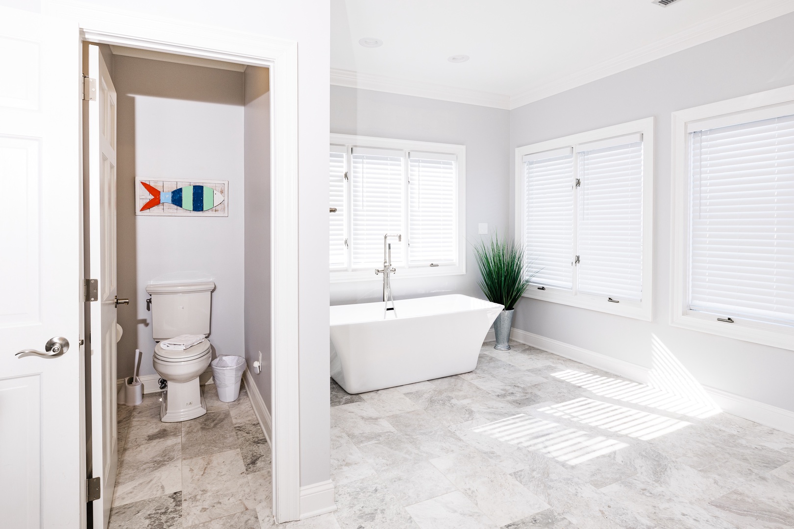 Unwind in your bright, modern bathroom with a luxurious freestanding tub surrounded by natural light from multiple windows.