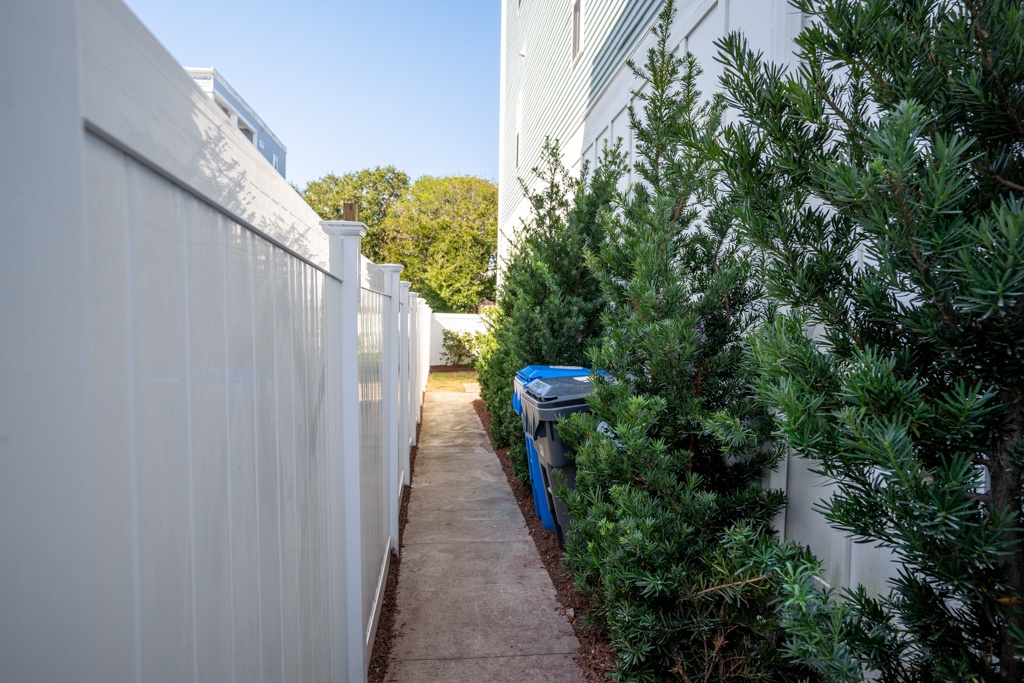 Side walkway leading to the backyard, bordered by lush landscaping and a clean white fence for complete privacy.