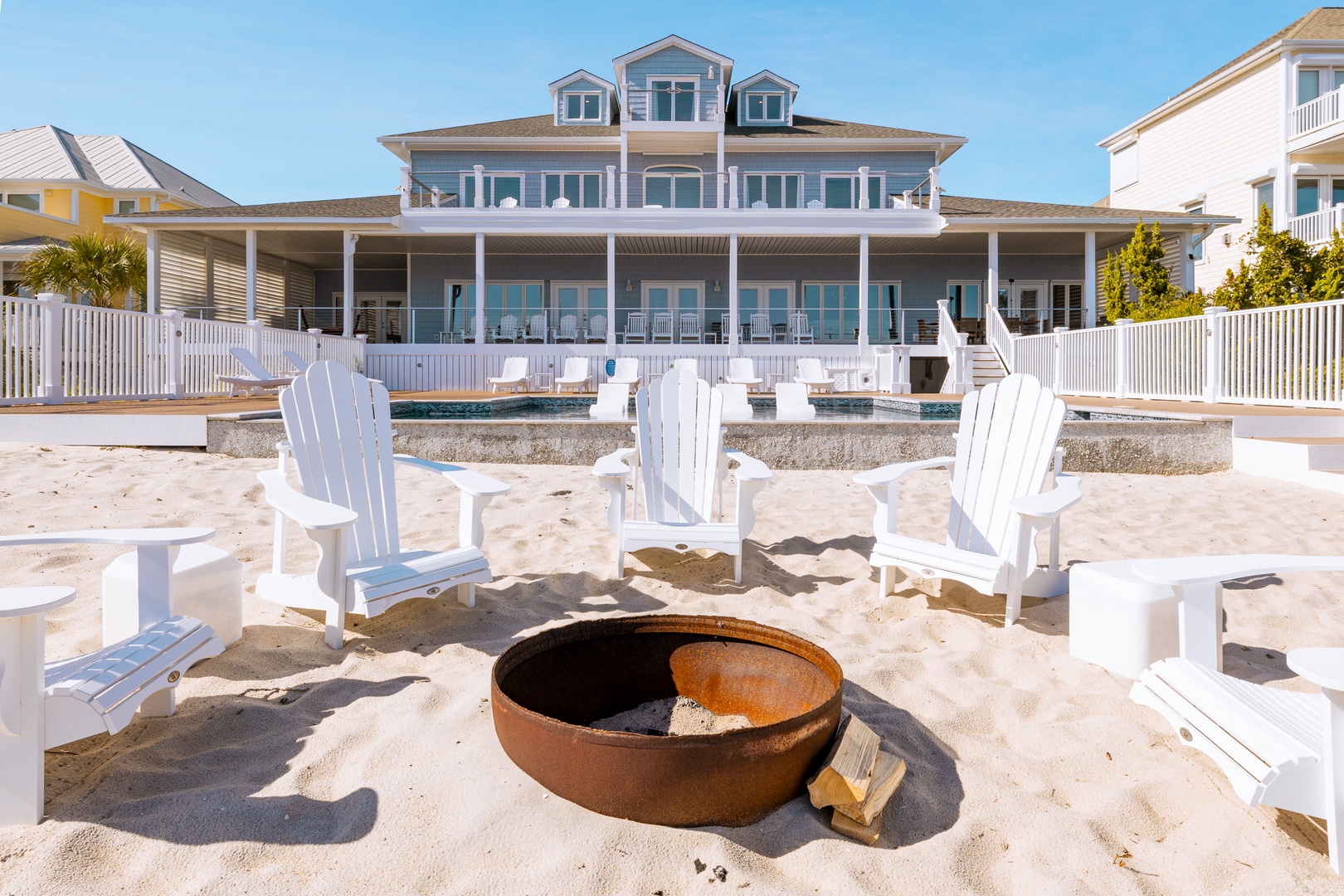 Beachfront property featuring a large coastal home with wraparound deck, swimming pool, and private beach access with fire pit seating area.