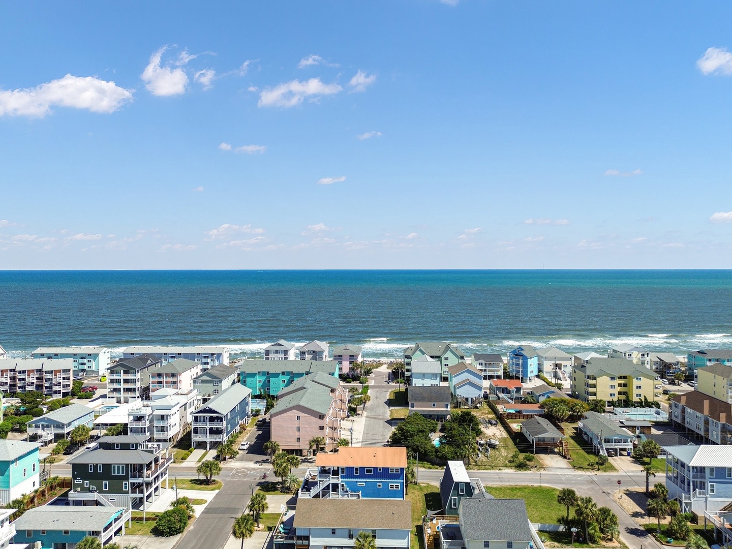 Aerial view of colorful beachfront vacation rentals stretching along pristine coastline with azure waters and sandy shores.