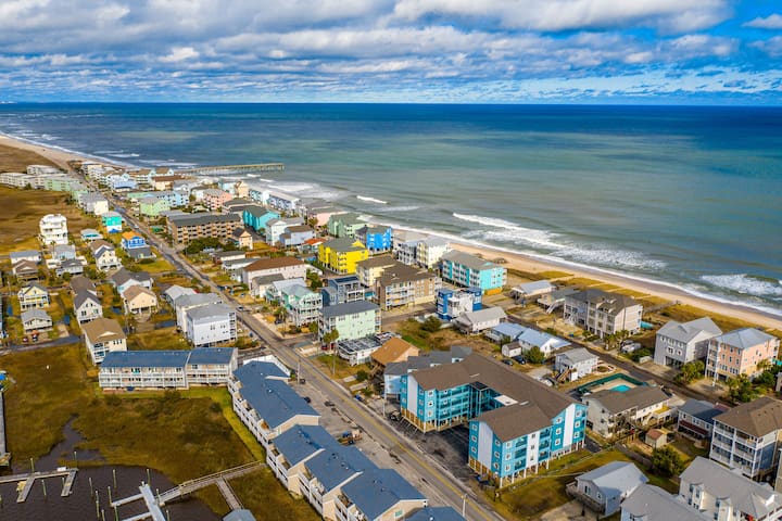 Coastal community with oceanfront homes stretching along pristine sandy beaches under dramatic cloudy skies.