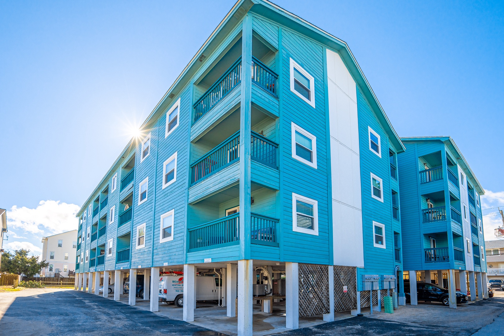 Vibrant turquoise coastal building featuring modern architecture with covered parking and multiple balconies under clear blue skies.