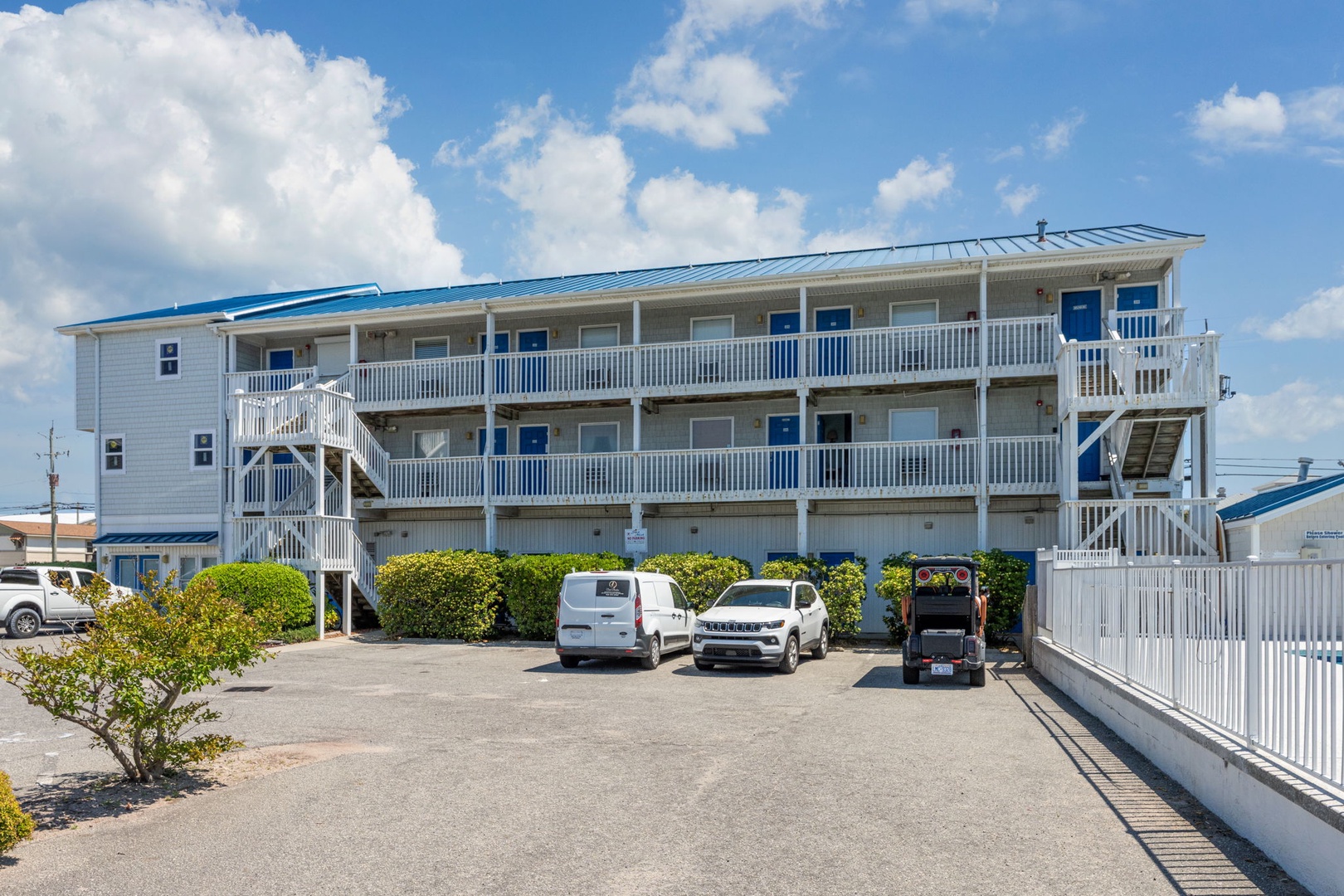 Multi-level coastal property with blue accents and convenient parking area for guest arrivals.
