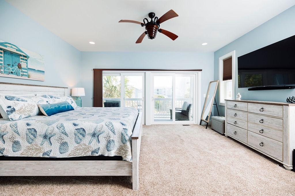 Your coastal-themed bedroom features a comfy bed with shell-patterned linens, ceiling fan, TV, and private balcony access.