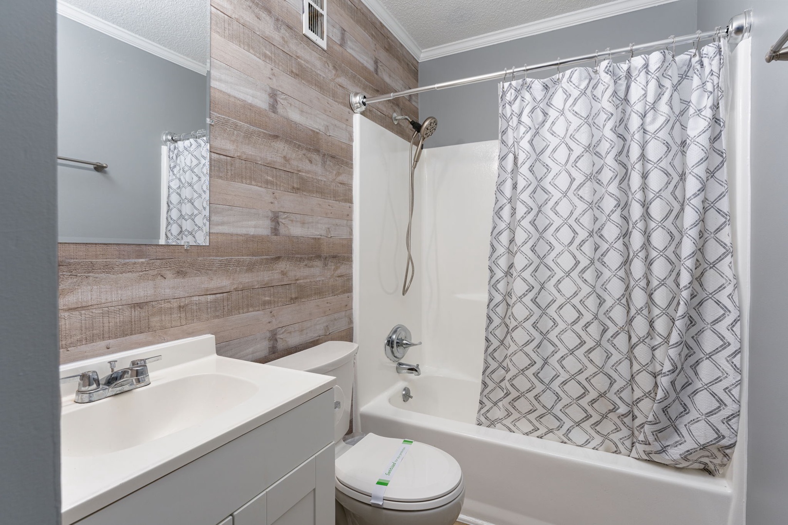 Freshen up in your private bathroom featuring a walk-in tub-shower combo, modern vanity, and stylish wood-look accent wall that adds warmth to the space.