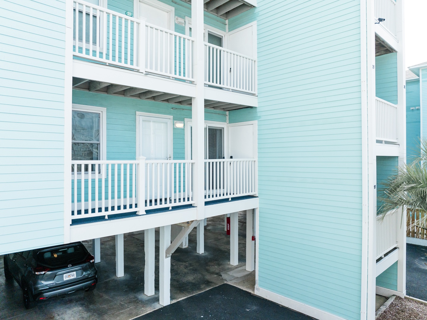 Charming turquoise coastal building with covered parking and private balconies in a tropical setting.