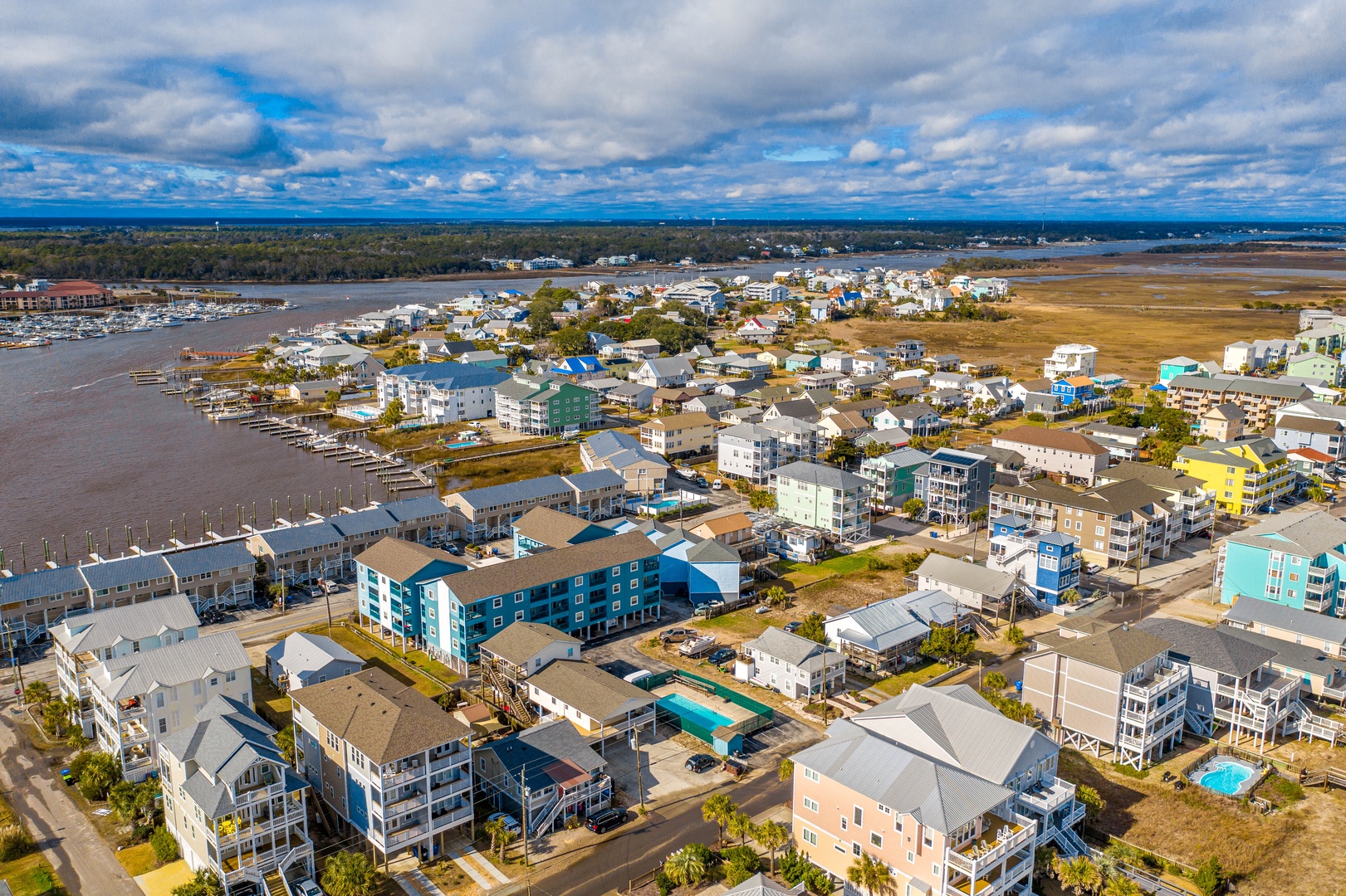 Aerial view of a vibrant coastal community featuring colorful vacation rental homes, private pools, and marina access along the waterfront.