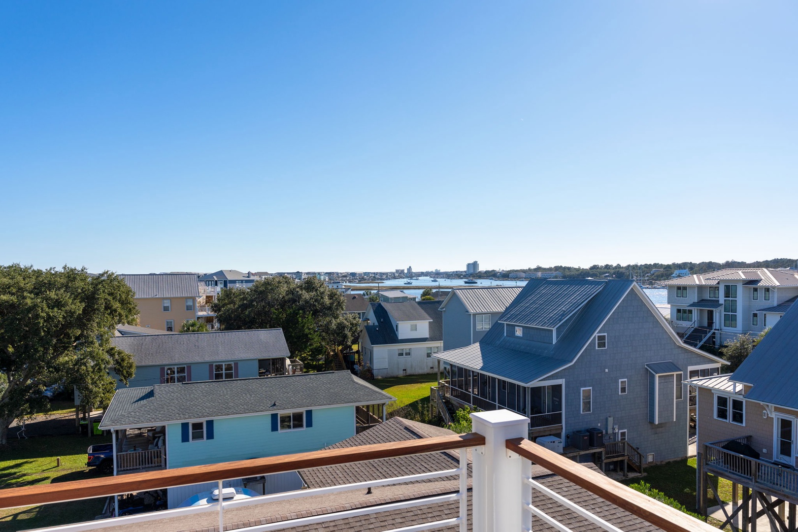 Elevated deck view showcasing coastal neighborhood homes with water glimpses in the distance under clear blue skies.
