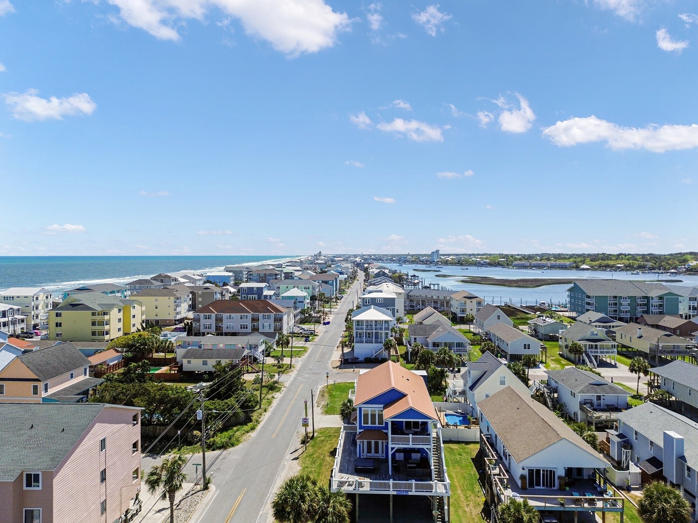 Aerial view of coastal community with charming beach houses, waterfront access, and scenic ocean views stretching to the horizon.