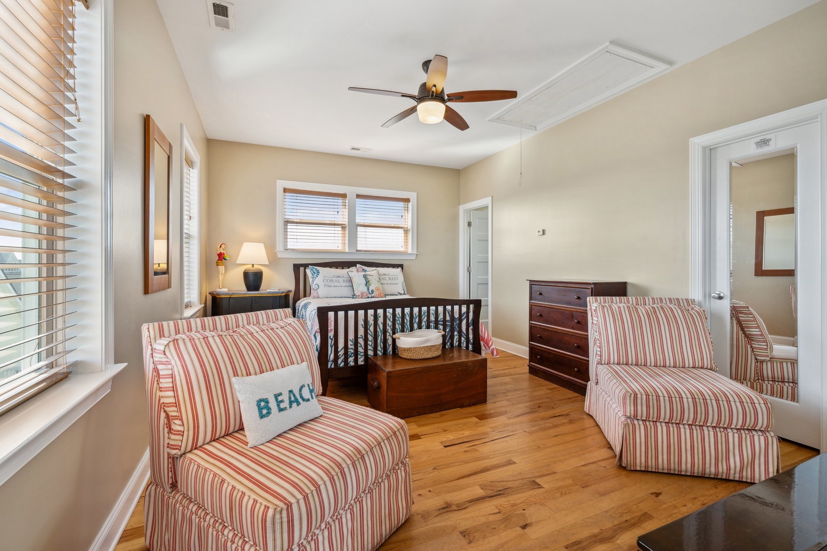 Relax in your cozy bedroom featuring comfortable striped armchairs, warm wood floors, and a ceiling fan for perfect comfort during your stay.