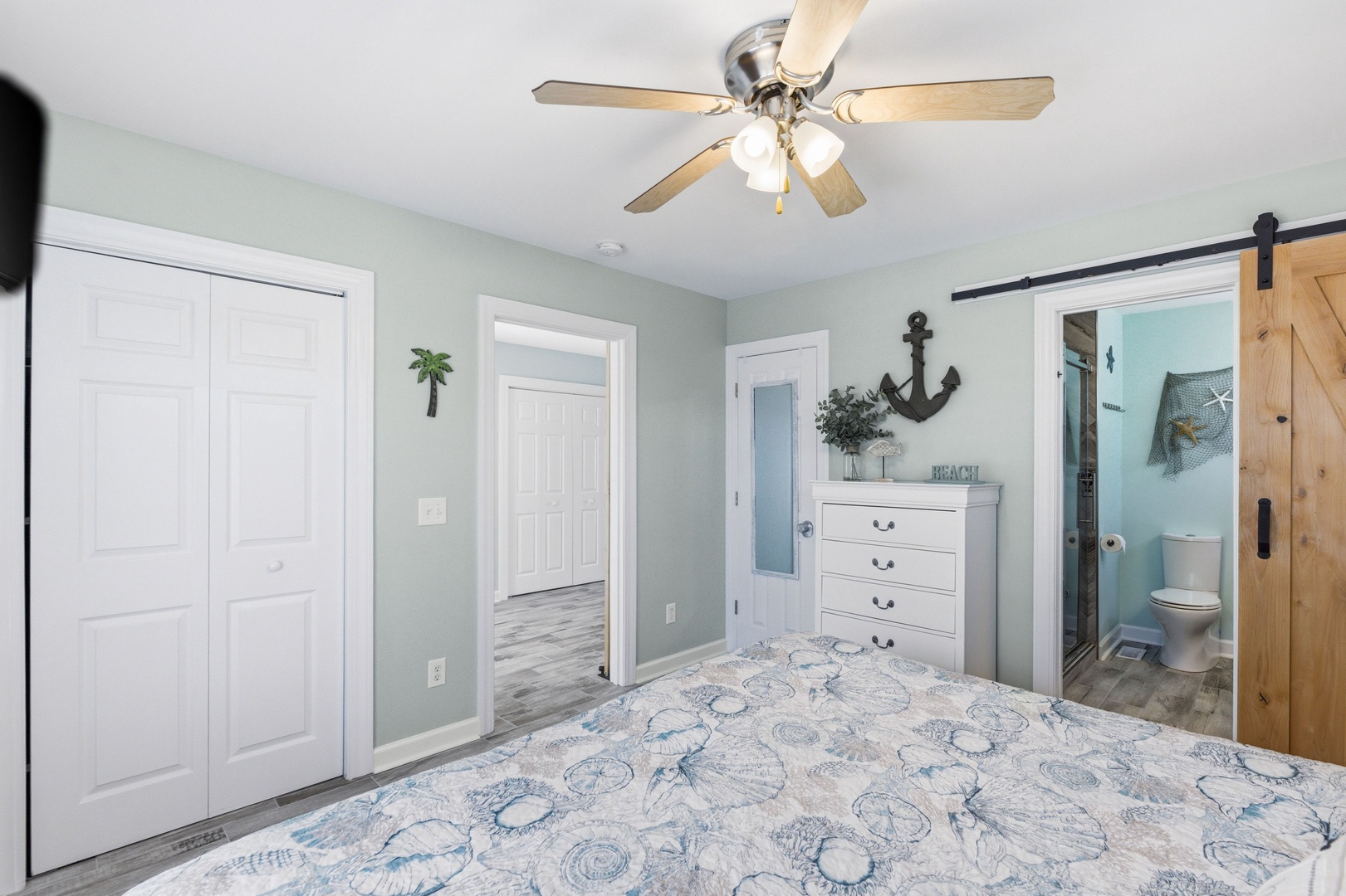 Your coastal-inspired bedroom awaits with soothing sea-green walls, a ceiling fan for gentle breezes, and a charming nautical theme—complete with a barn door leading to your private bathroom.