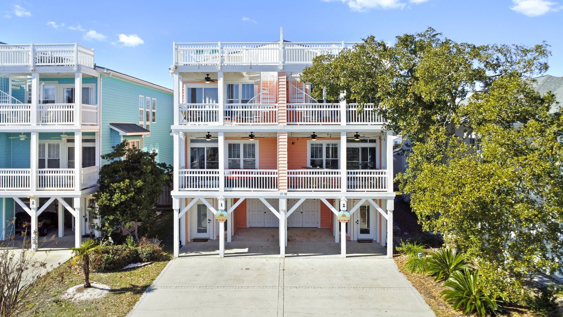 Charming coral-colored beach house with white railings and multiple balconies in coastal neighborhood.
