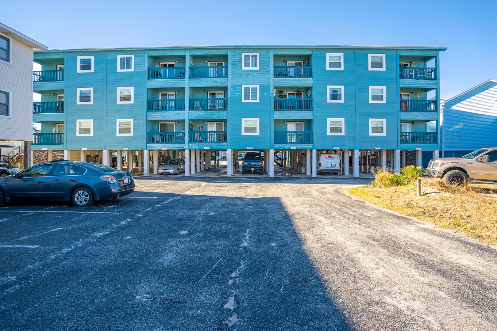 Bright turquoise beachside building with covered parking and private balconies for each unit.