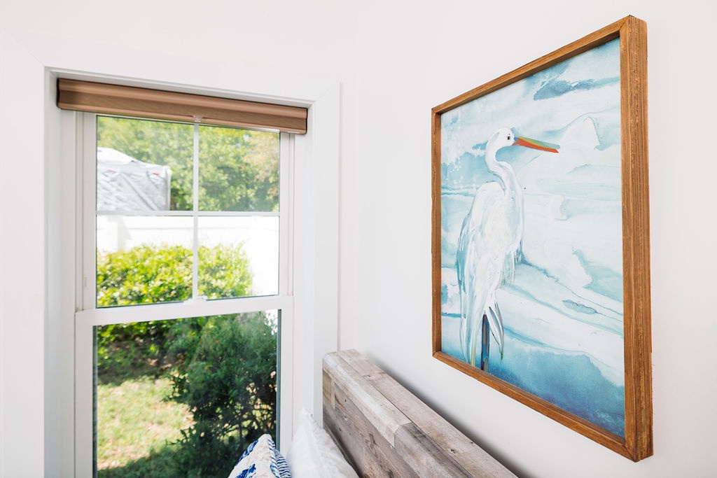 Relax in your thoughtfully decorated bedroom where coastal artwork and garden views create a peaceful retreat for unwinding.