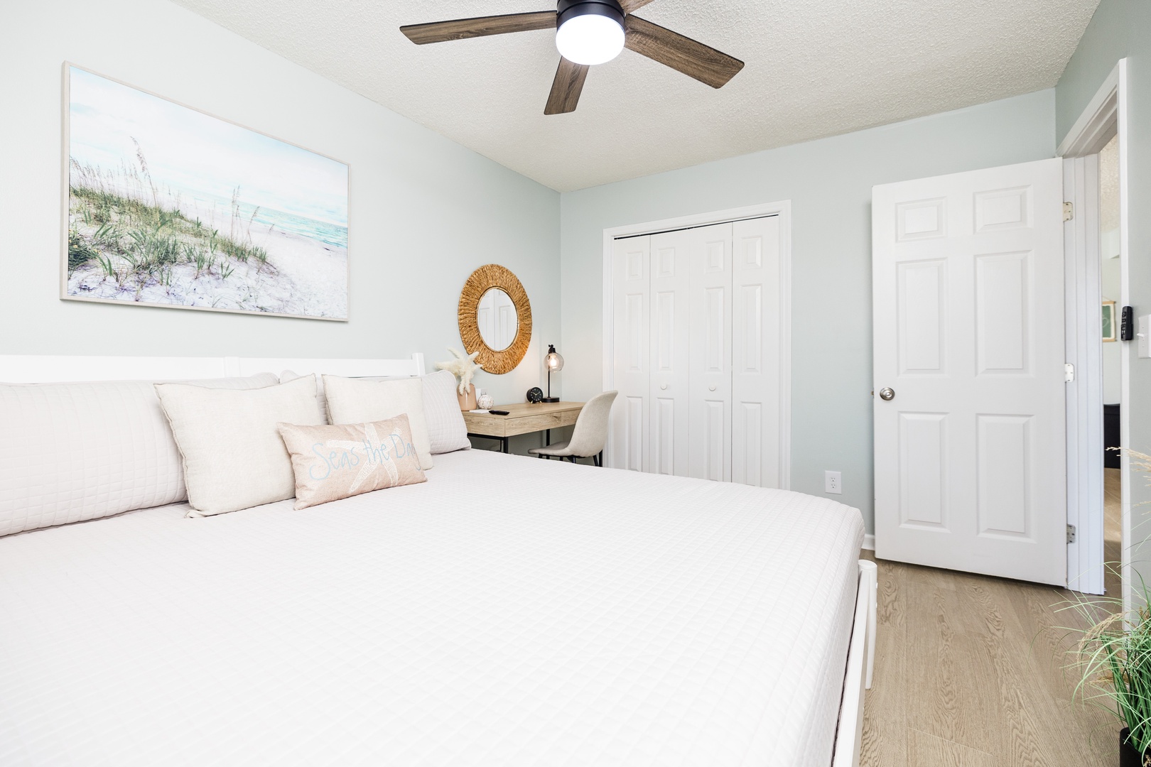 Your peaceful bedroom features a cozy queen bed, dedicated workspace, and coastal charm with beach artwork and warm natural light.