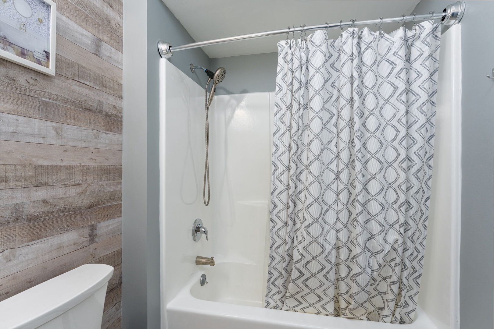 A modern bathroom featuring a tub-shower combo with stylish geometric curtain, sleek fixtures, and soothing coastal blue walls. Perfect for refreshing after your daily adventures.