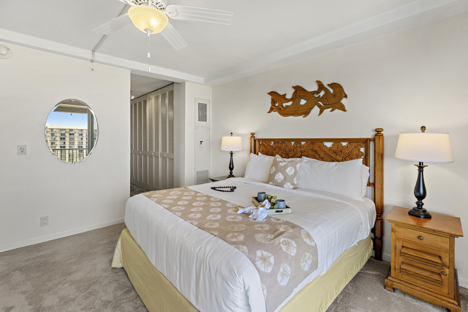 Your coastal retreat awaits with a plush king bed, tropical carved-wood accents, and a circular window framing bright island views—rest easy here.