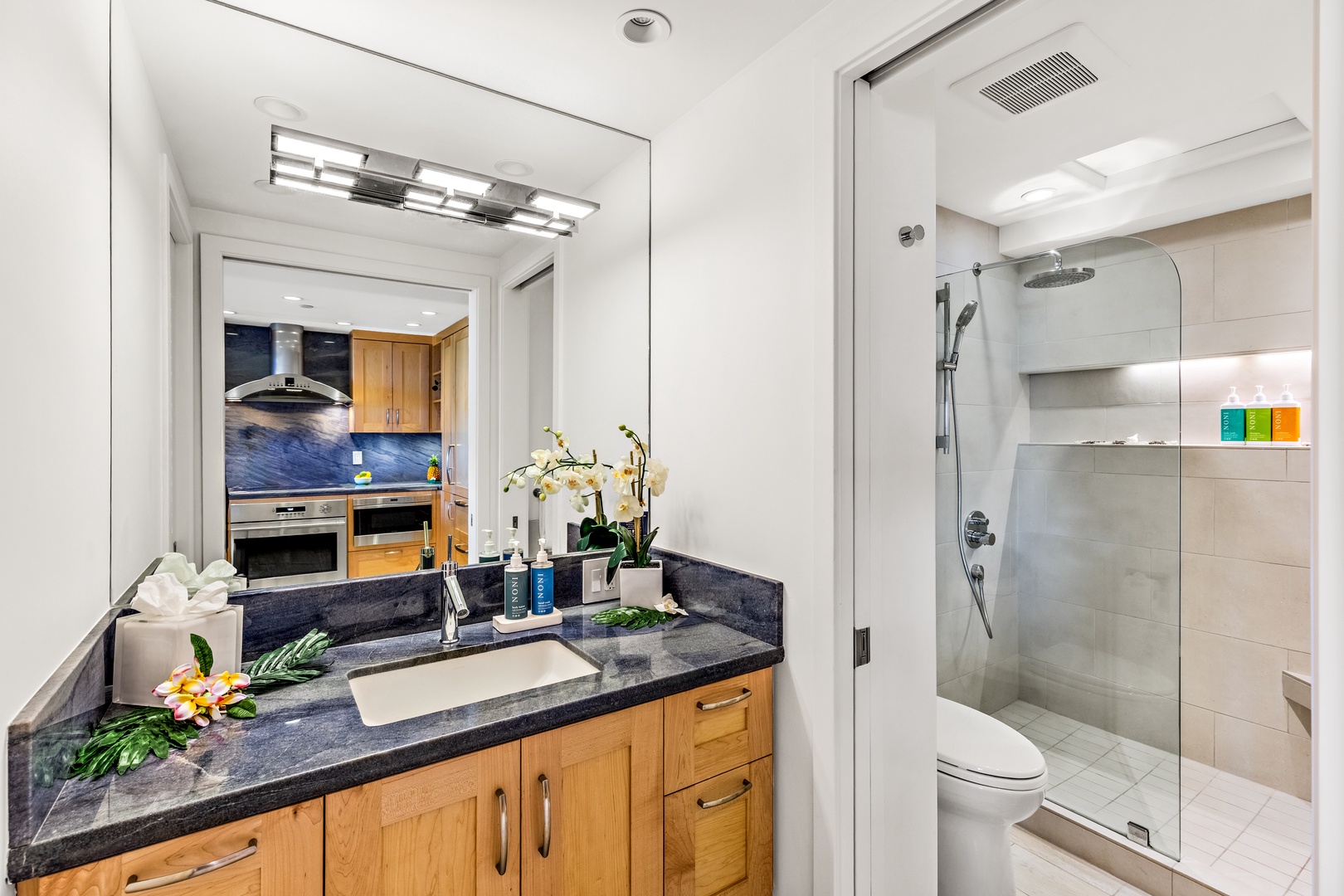 Your private bathroom offers a sleek vanity with dark granite counters and a spacious walk-in shower with rainfall and handheld showerheads for ultimate comfort.