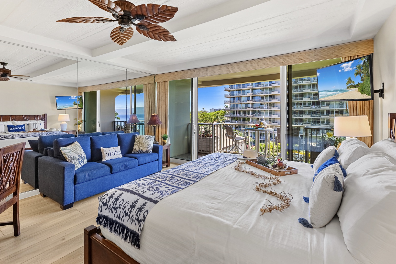 Your tropical bedroom suite features crisp white linens and vibrant blue accents, with floor-to-ceiling windows framing stunning ocean views.