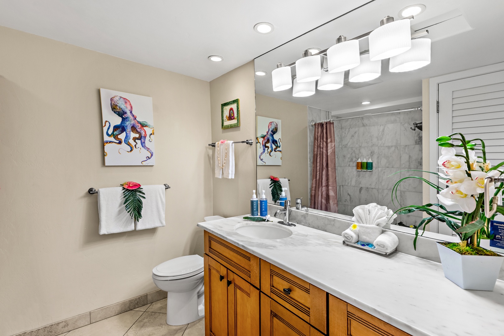 Refresh in your elegant bathroom featuring a spacious marble countertop, warm wood cabinetry, and vibrant ocean-themed artwork.