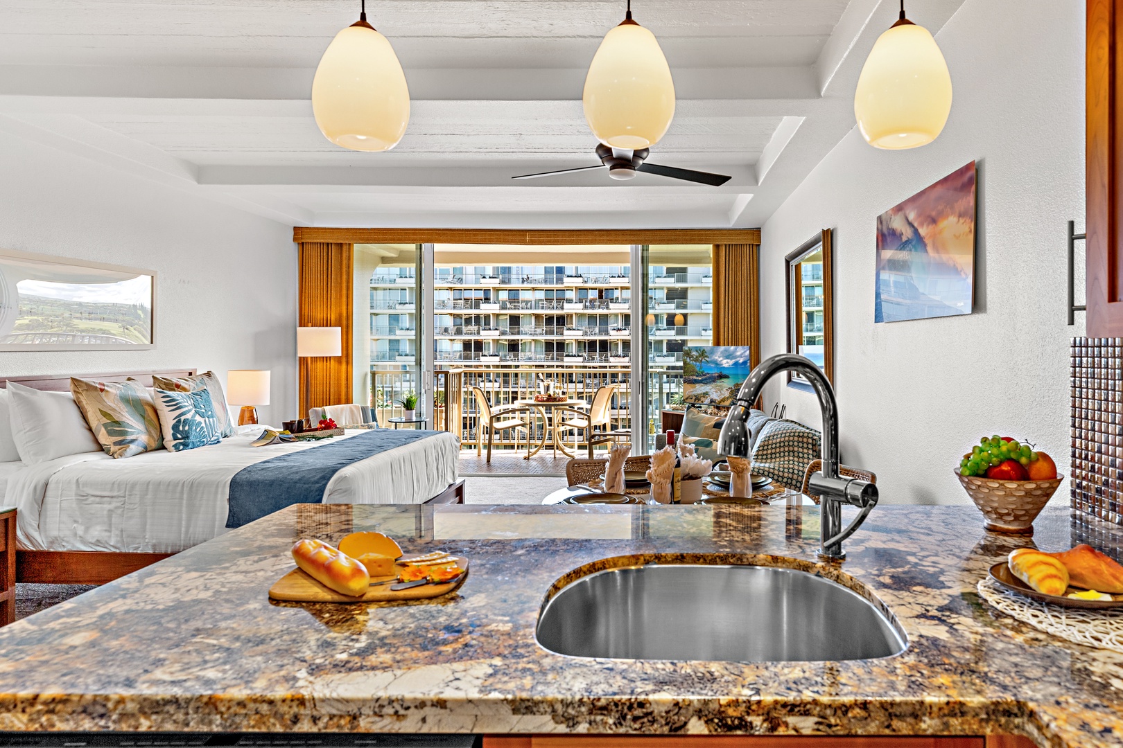 Spacious suite blending bedroom comfort with a sleek kitchen. Fresh fruit awaits, pendant lights glow warmly, and your private balcony opens to scenic views—perfect for relaxed mornings or breezy evenings.