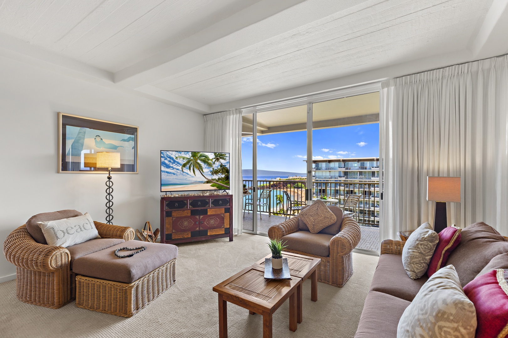 Unwind in your spacious living room where rattan chairs and a plush sofa invite you to relax, while the open balcony door frames sweeping ocean views and gentle coastal breezes.