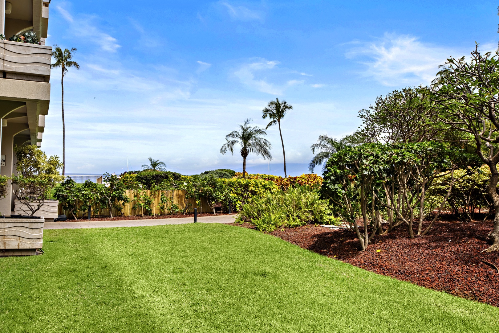 Manicured grounds feature lush tropical landscaping with palm trees and ocean views beyond the garden.