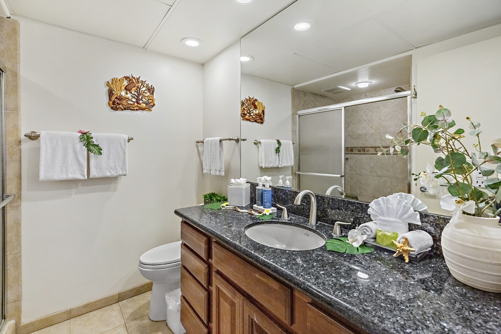 Step into your spacious bathroom featuring sleek granite countertops, rich wood cabinetry, fresh towels, and a beautifully tiled walk-in shower—your private spa awaits.