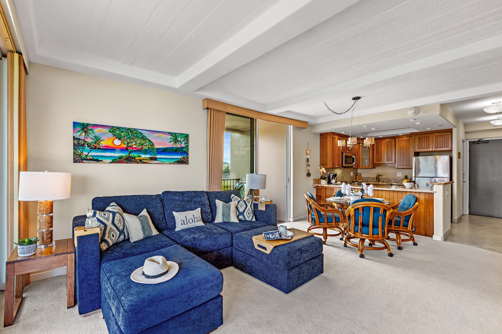 Relax in your tropical-themed living space with plush seating and a fully equipped kitchen, all under soaring white beam ceilings.
