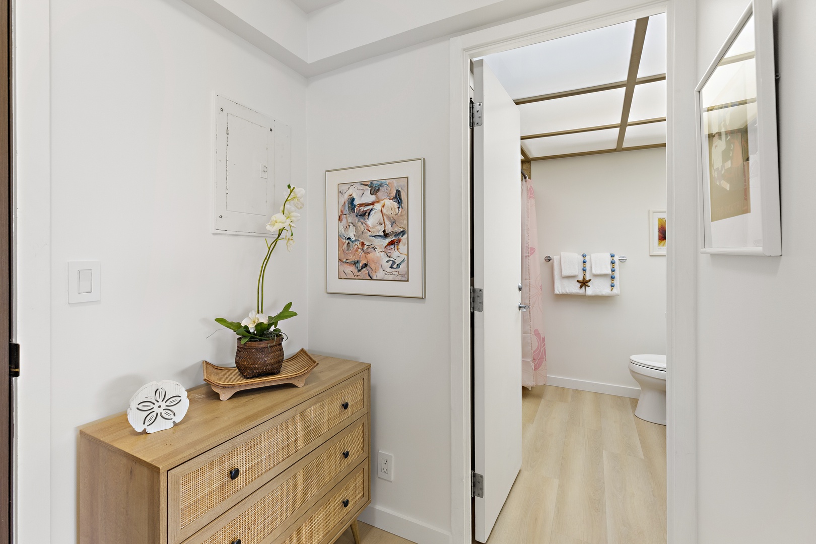 Your ensuite bathroom awaits just steps from your sleeping space, featuring a spacious shower and elegant fixtures. The adjoining entry space offers convenient storage with stylish built-in shelving and a charming dresser topped with fresh orchids.