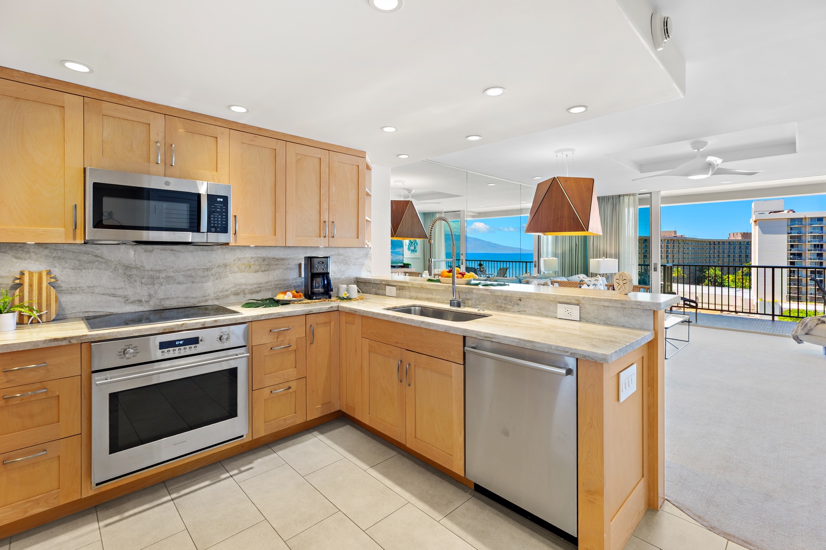 Your fully equipped kitchen features modern appliances, sleek countertops, and warm wood cabinetry—perfect for preparing meals while enjoying stunning ocean views through the open living space.